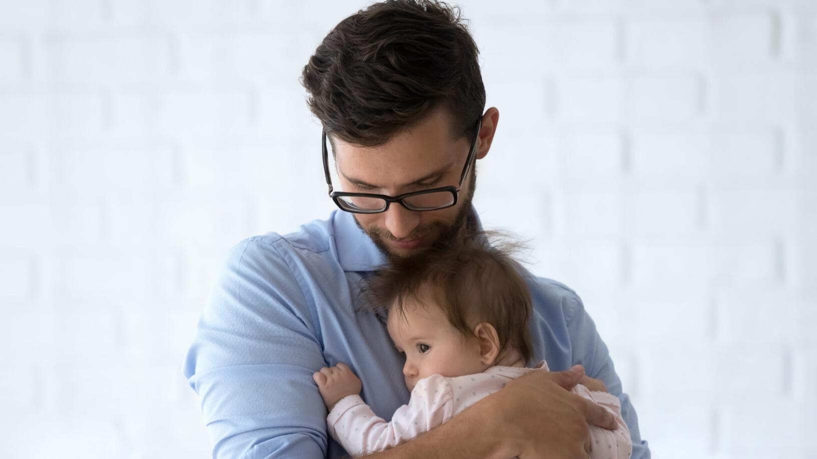 Um homem míope com óculos a segurar um bebé.