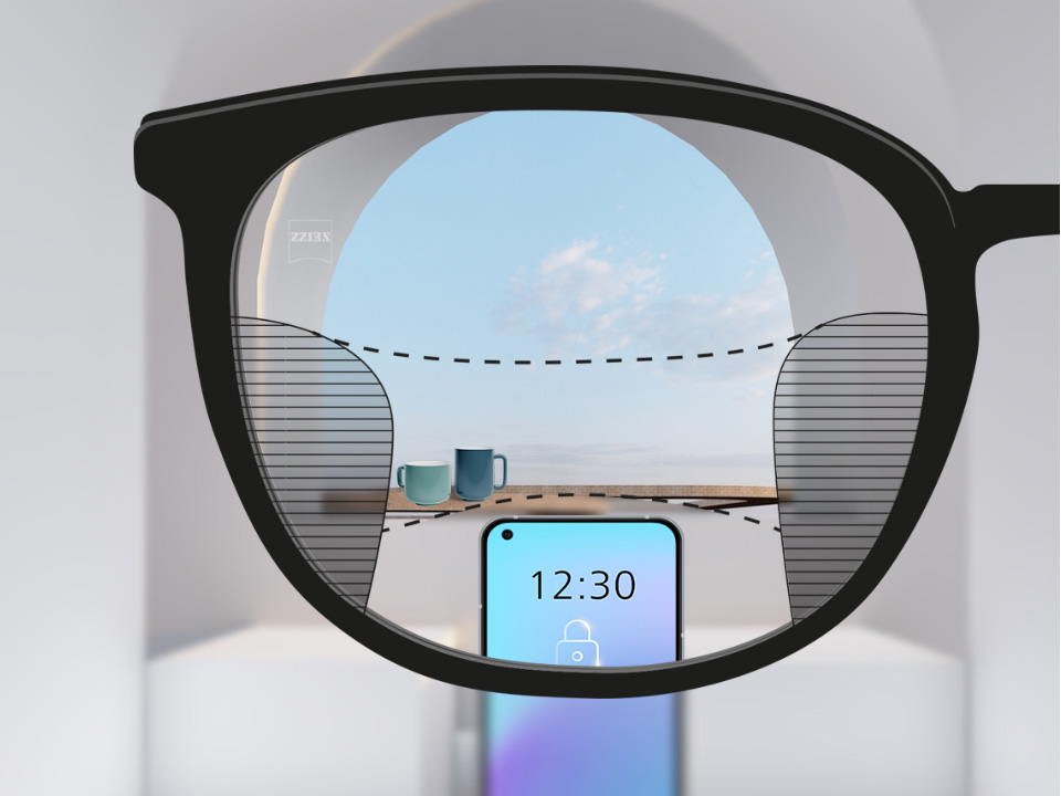 Imagem de um smartphone e de chávenas em segundo plano através da lente ZEISS SmartLife Progressiva, que está totalmente nítida, mas com finas parcelas desfocadas à esquerda e à direita.