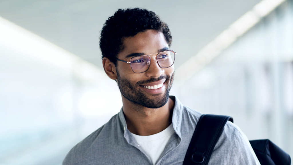 Um jovem a sorrir de mochila ao ombro, a usar óculos com lentes ZEISS SmartLife Digital e a olhar para o lado.