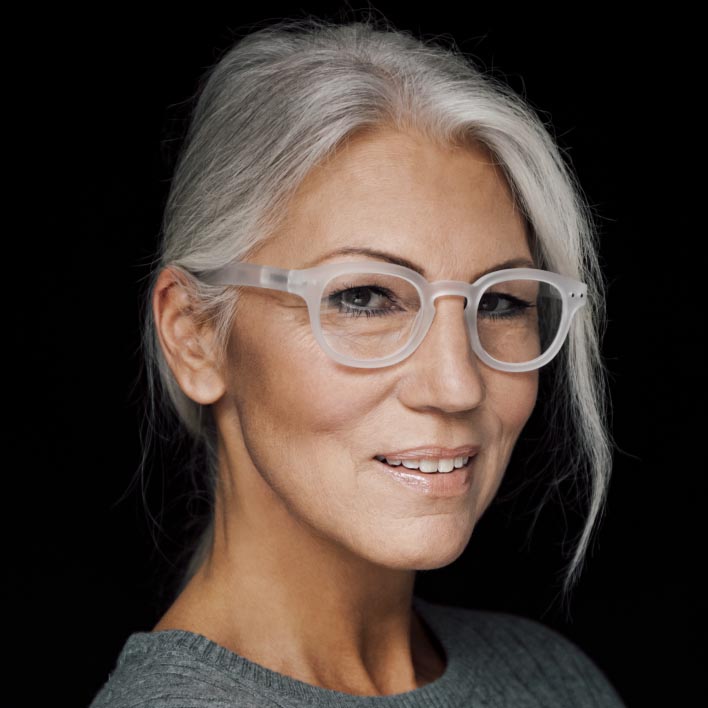 Mulher com cabelo grisalho a usar uma armação branca com lentes ZEISS SmartLife Progressiva. Digitalização geométrica do rosto que mostra a anatomia facial e as medidas da armação.